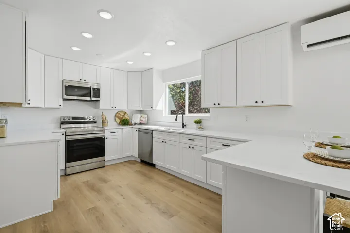 Modern kitchen featuring white cabinetry, stainless steel appliances, light-toned wood-type LVP flooring, recessed lighting, and a window with natural light