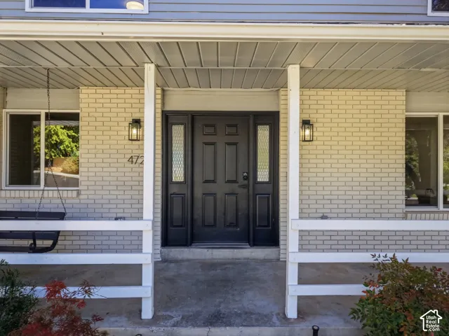 Covered porch and entryway with brick facade, black paneled door with decorative glass sidelights, and two exterior sconces