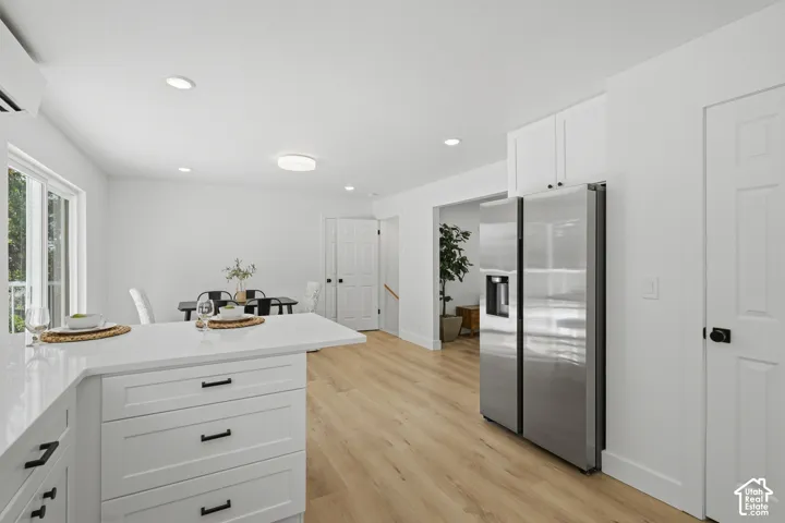 Kitchen island with white cabinetry and dark hardware, stainless steel refrigerator, light wood-finish flooring, recessed lighting, and a pantry