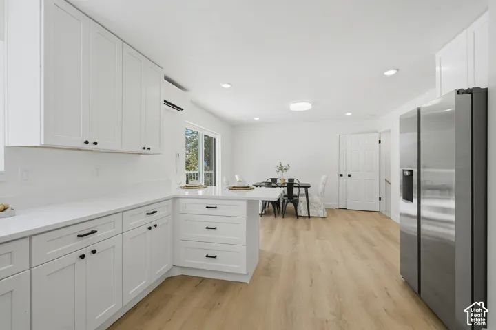 White shaker cabinetry, light wood-finish LVP flooring, stainless steel French door refrigerator, white quartz countertops, and a sliding glass door