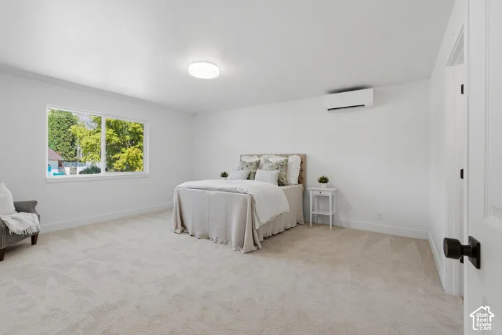 Primary bedroom with neutral carpeting, large windows, recessed lighting, and a wall-mounted climate control unit