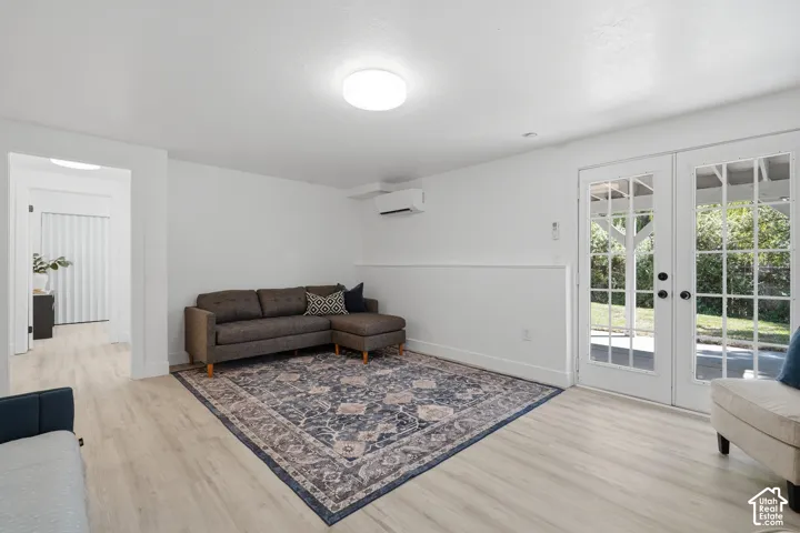 ADU living room with light-toned laminate flooring, white walls, white French doors, and a wall-mounted mini-split unit