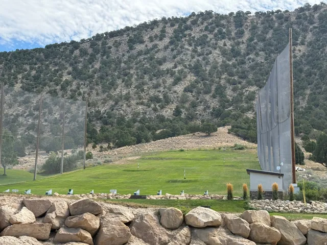 Driving range featuring multiple hitting bays, a putting green, and a rock retaining wall