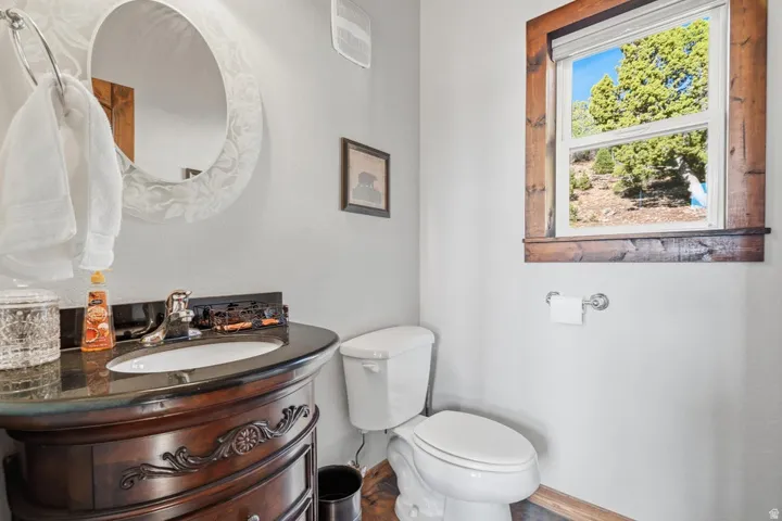 Vanity with a dark countertop and undermount sink, circular decorative mirror, and a window with a wood frame