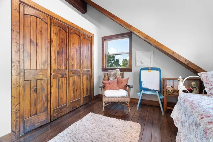 Sloped ceiling with exposed wood beams, wood-finish flooring, wood-framed window, and wood bifold doors
