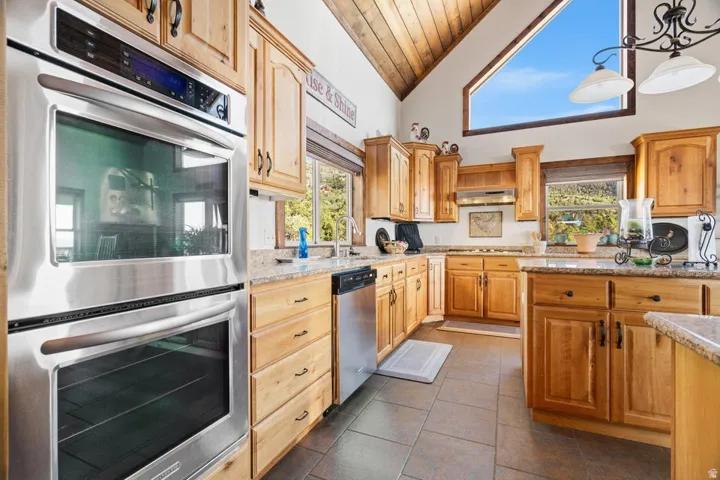 Vaulted wood-paneled ceiling, stainless steel double wall ovens, wood cabinetry, granite-style countertops, and a large triangular window