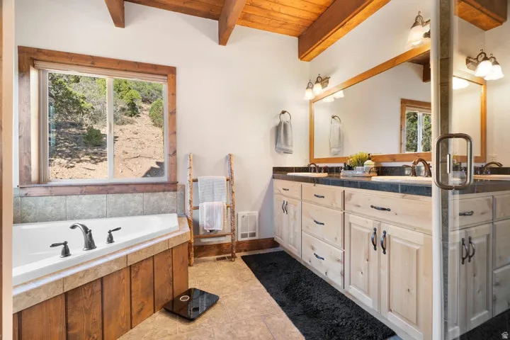 Vaulted wood-beam ceiling, dual vanity with undermount sinks, and a large soaking tub