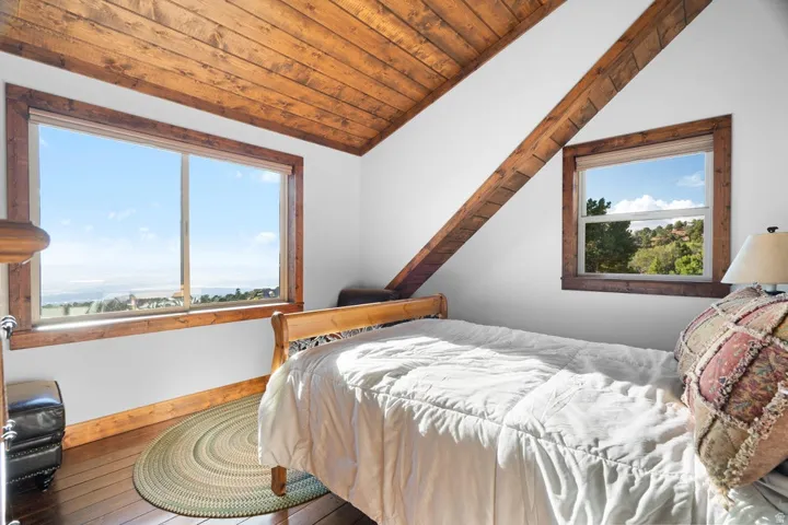 Vaulted wood-paneled ceiling, exposed wood beams, wood-finish flooring, large window, and secondary window