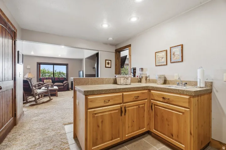 Wet bar with light wood cabinetry, stone-finish countertops, and an integrated sink