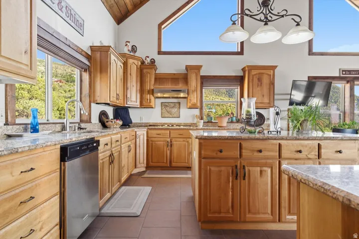 Kitchen featuring wood cabinetry, light-toned countertops, stainless steel dishwasher, tile flooring, and vaulted ceiling with exposed wood beams