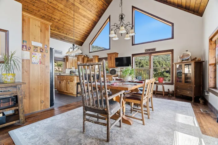 Vaulted wood-finish ceiling, large triangular windows, wood-finish flooring, kitchen with wood-finish cabinetry, and built-in display cabinet