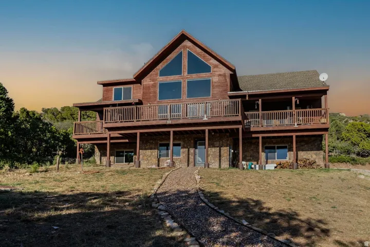 Cedar-clad exterior with a stone foundation, multiple balconies, a gravel path, and prominent A-frame windows