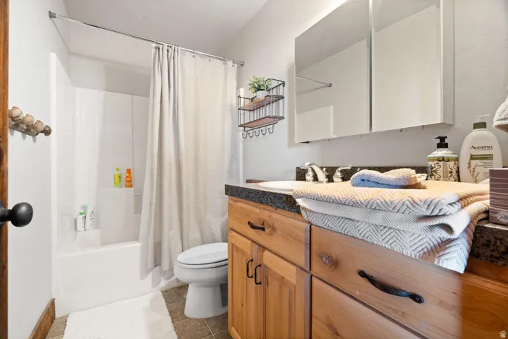 Bathroom featuring a shower/tub combination, wood-finish vanity with dark countertop, surface-mounted sink, wall-mounted medicine cabinet, and tile flooring