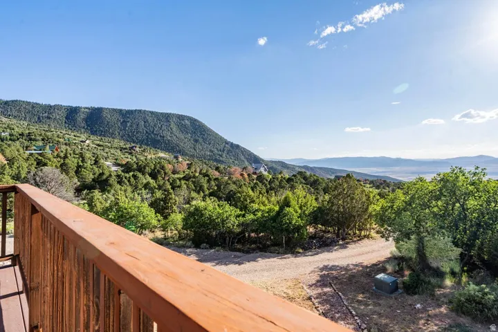Wood-finish deck railing with a natural wood deck surface, overlooking a mountainous landscape with distant valleys and abundant mature trees