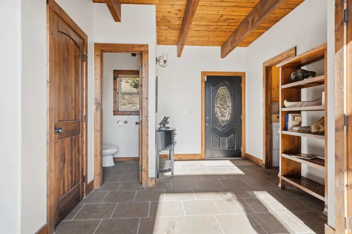 Textured tile flooring, exposed wood beam ceiling, paneled wood doors, decorative front door, built-in wood shelving