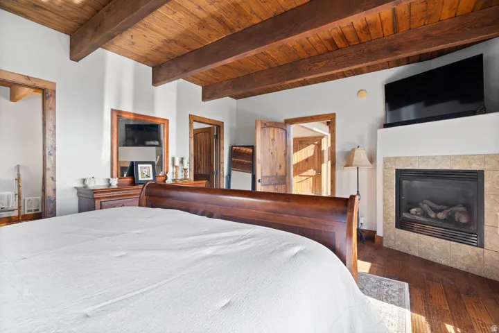 Wood-finish flooring, exposed wood beam ceiling, tiled fireplace with hearth, and wood-paneled doors
