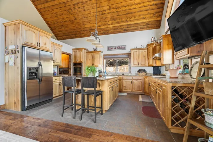 Vaulted wood-paneled ceiling, wood-finish cabinetry, granite countertops, stainless steel appliances, and tile flooring