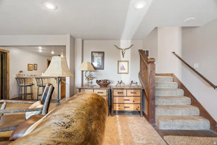 Carpeted staircase with wood handrail, recessed lighting, and a wood-paneled bar area