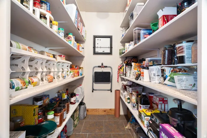 Spacious pantry featuring extensive shelving, durable tile flooring, and a decorative wood baseboard