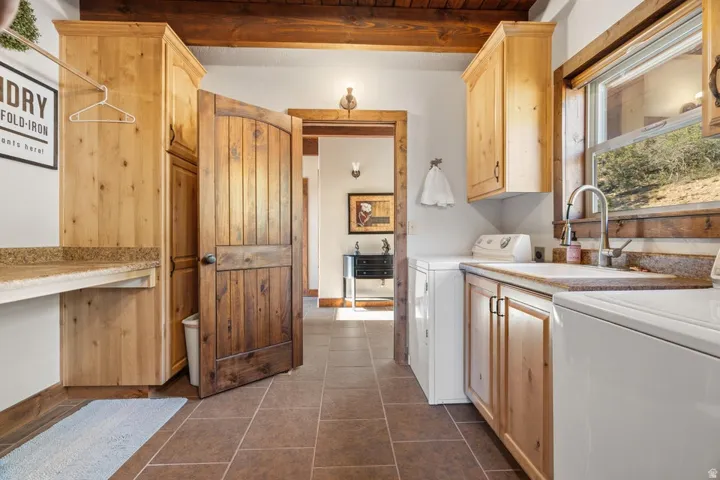 Laundry area with wood-finish cabinetry, a utility sink, and a window with wood trim