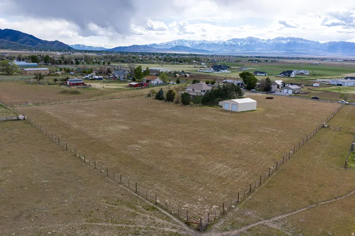 Expansive land parcel with surrounding fencing, a two-bay metal outbuilding, and distant mountain backdrops
