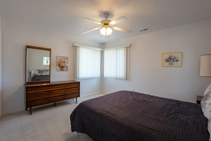 Corner windows with horizontal blinds, ceiling fan with integrated lighting, and neutral wall tones
