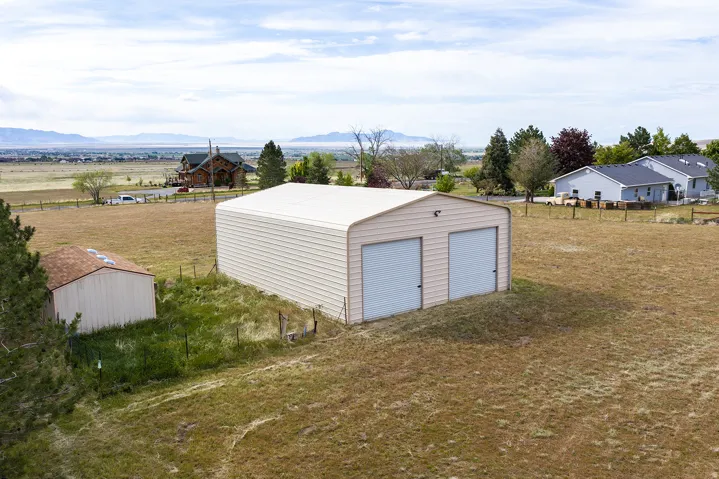 Two-door detached garage with metal siding, accompanied by a separate storage shed, situated on a spacious, grassy lot