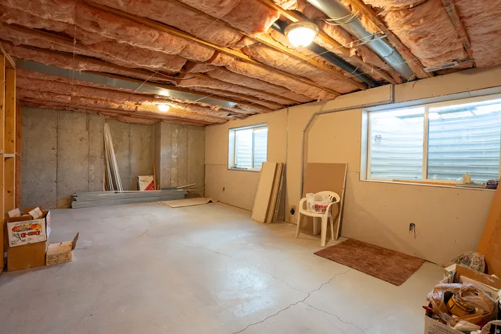 Unfinished basement with concrete flooring, exposed ceiling joists, and multiple windows
