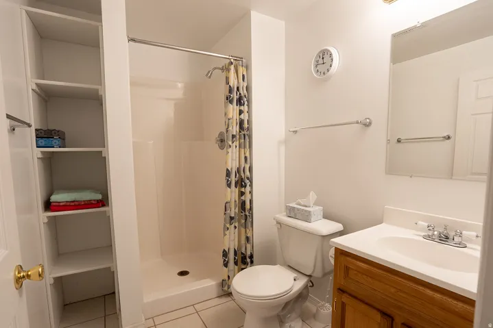 Walk-in shower with white surround, built-in shelving, wood-finish vanity with an integrated sink, and a mirrored medicine cabinet