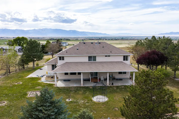 Two-story stucco residence with a covered patio, multiple windows, and a shingled roof
