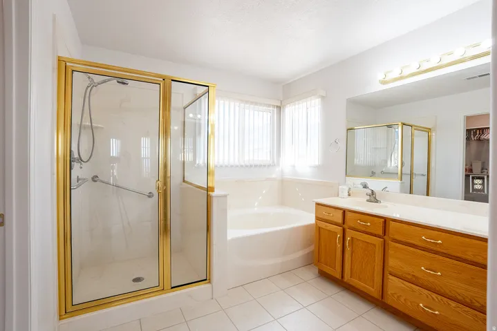 Expansive bathroom featuring a gold-framed glass shower, built-in soaking tub, wood-finish vanity with countertop, and large wall-mounted mirror