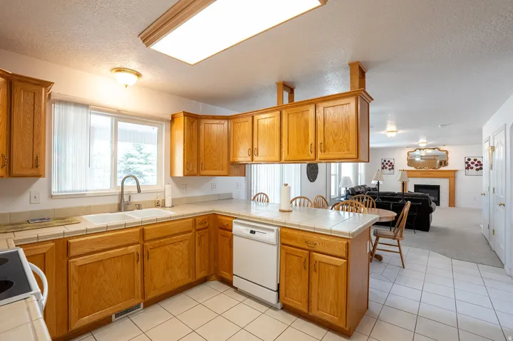 Kitchen with wood cabinetry, white tile flooring, white tile countertops, and a double basin sink with a gooseneck faucet