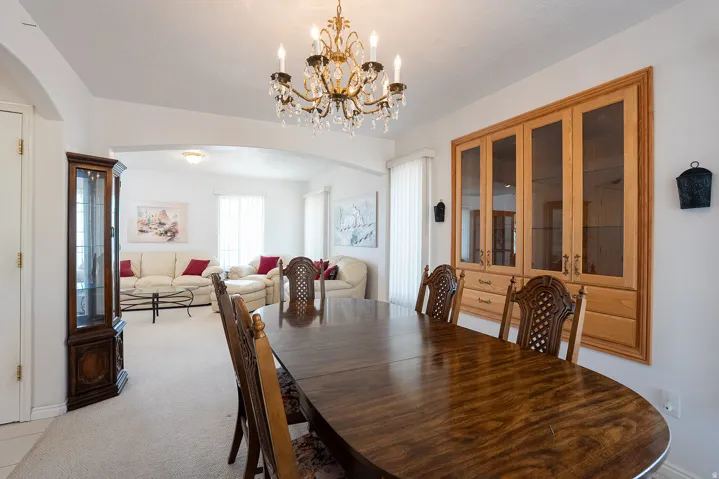 Formal dining space featuring a wood-finish dining table and matching chairs, an ornate crystal chandelier, and a built-in wood-finish cabinet with glass panel doors