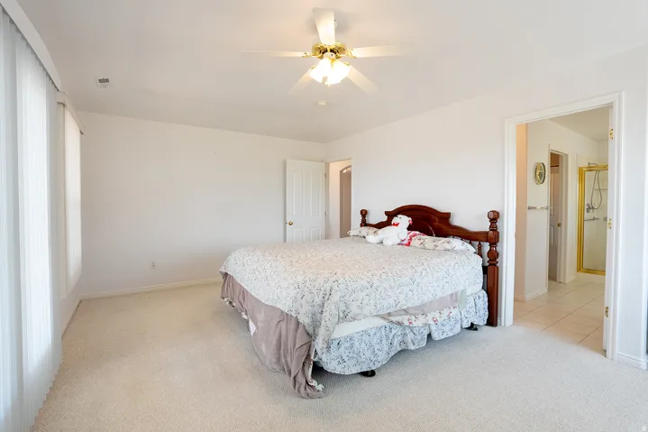 Wall-to-wall carpeting, overhead ceiling fan, white paneled doors, and an en-suite bathroom with a tiled shower