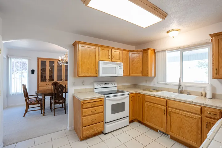 Kitchen featuring wood cabinetry, white tile flooring, white appliances, and a double basin sink