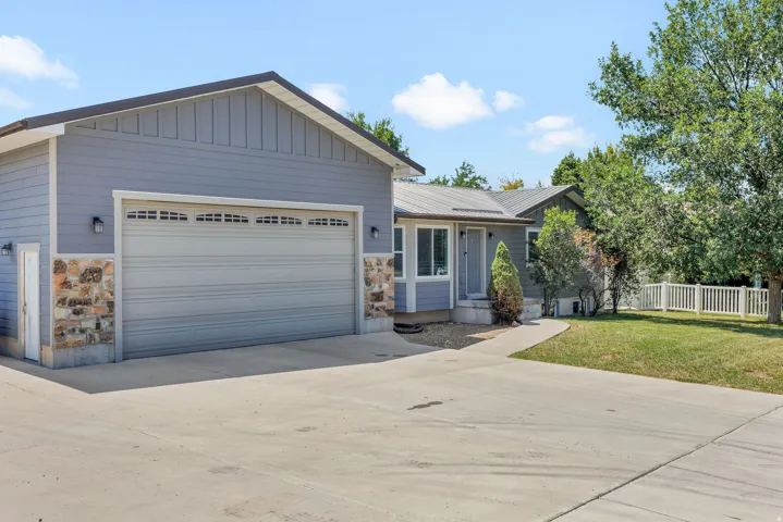 Attached two-car garage with stone veneer accents, light gray siding, and a side entry door