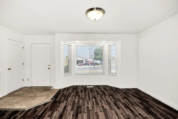 Bay window with blinds, wood-finish flooring, tiled entry, paneled interior door, and flush-mount ceiling light fixture