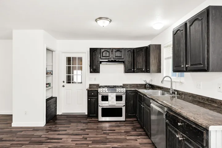 Kitchen featuring wood-finish flooring, dark wood cabinetry, stainless steel appliances, and a composite countertop