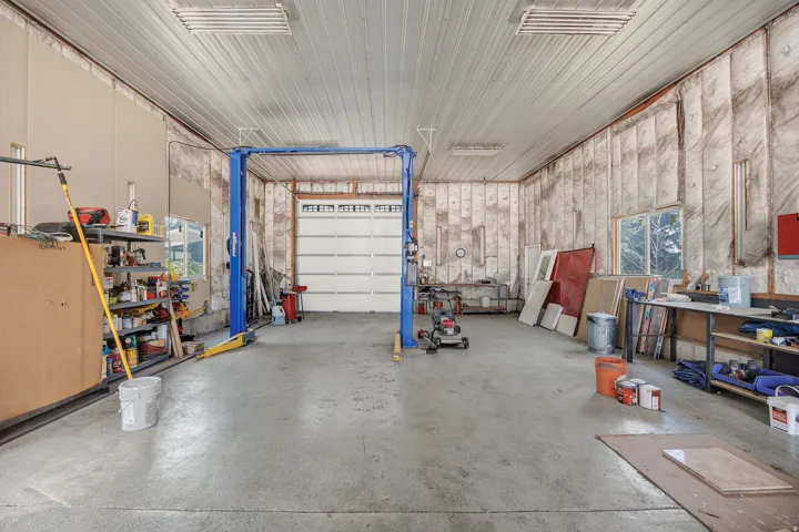 Expansive garage space with concrete flooring, high ceilings with exposed metal, and a large roll-up door