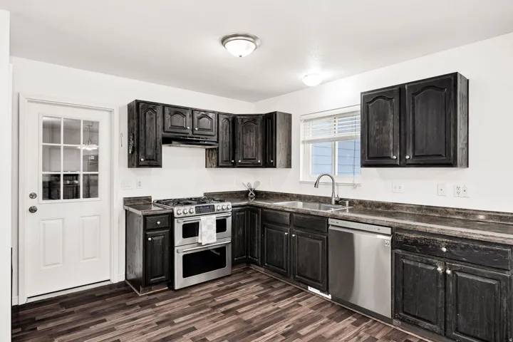 Kitchen featuring dark wood-finish cabinetry, stainless steel appliances, a five-burner gas range, a single basin sink with a gooseneck faucet, and wood-finish flooring
