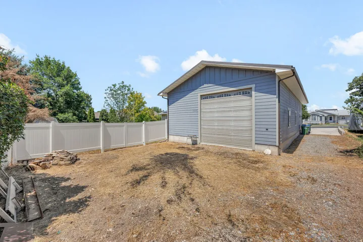 Detached structure with horizontal siding, a roll-up garage door, and a white vinyl fence