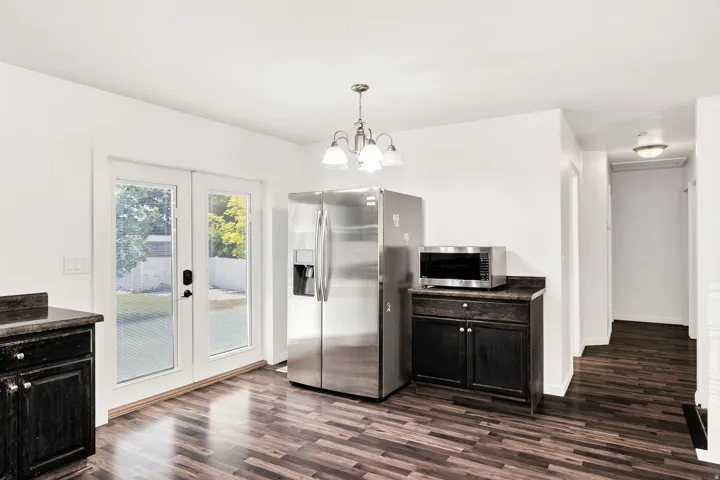 Wood-finish flooring, stainless steel French door refrigerator, dark wood cabinetry, and a three-light chandelier