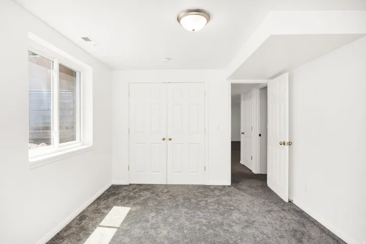 White walls with wall-to-wall carpeting, a large window, a ceiling-mounted light fixture, and a white double-door closet