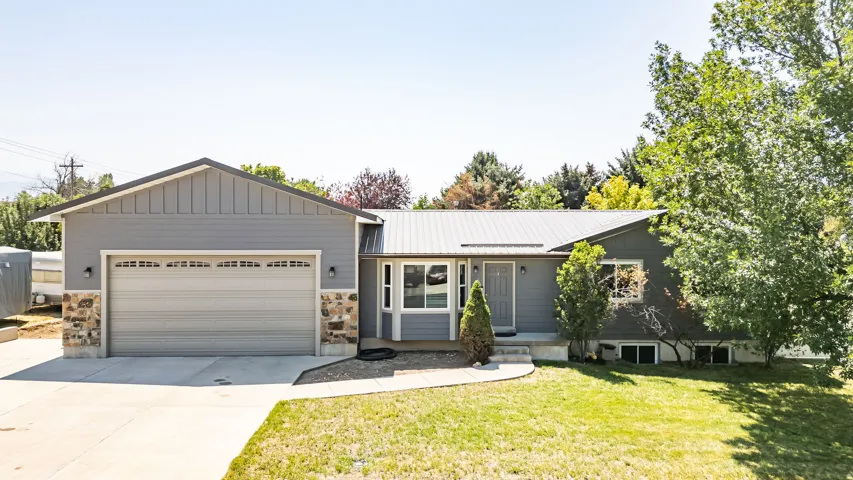 Exterior featuring a metal roof, attached garage, stone accents, and a paved driveway