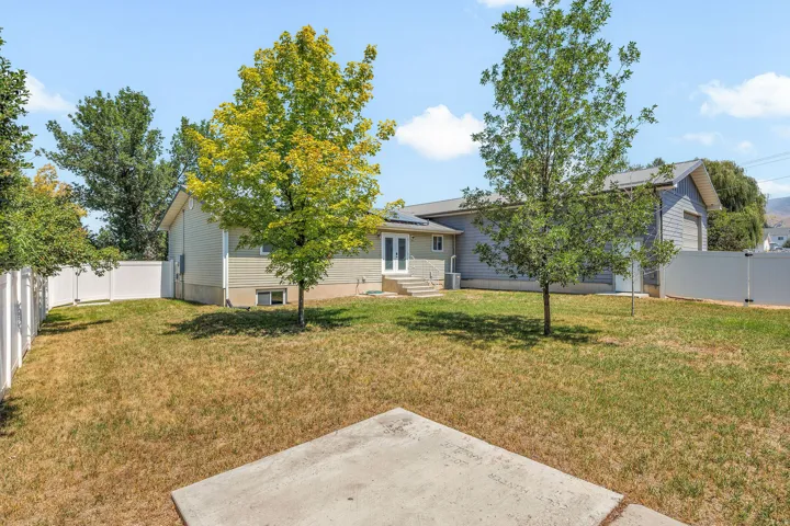 Fenced backyard with mature trees, a concrete patio, and a double door exterior entry