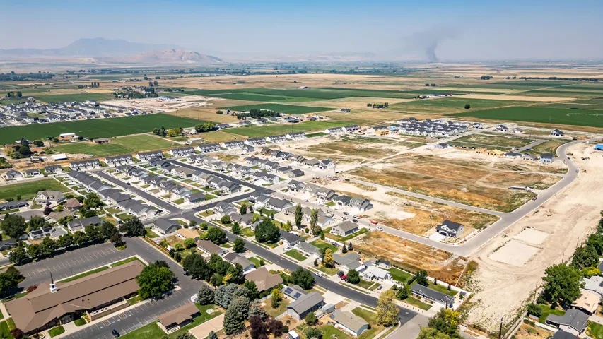 Aerial perspective showcasing an established neighborhood with mature landscaping, surrounded by open fields and distant mountains