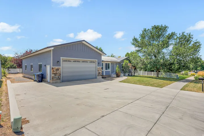 Detached garage with horizontal siding and stone accents, concrete driveway, front yard with mature trees, and a white picket fence
