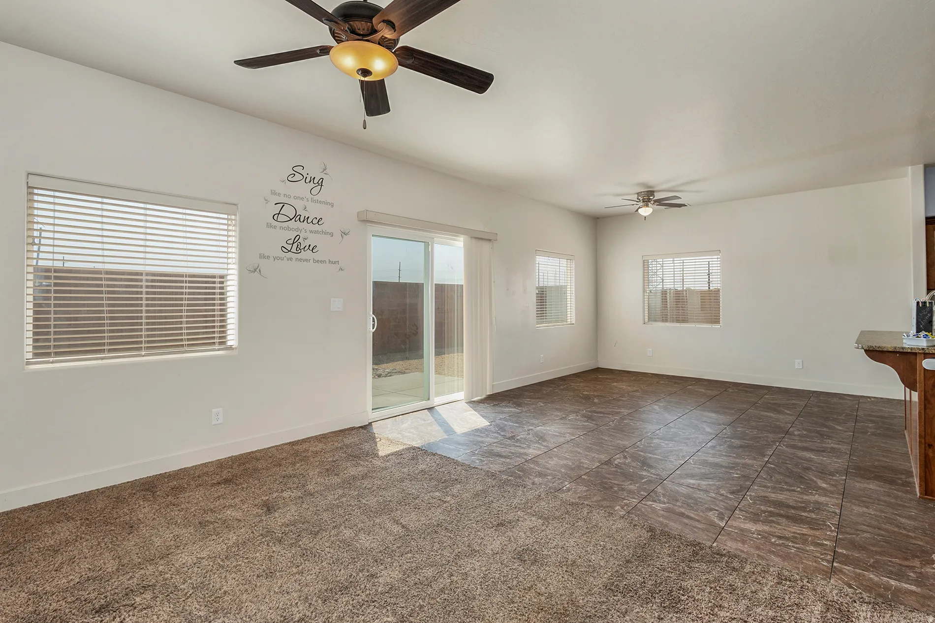 Spacious room featuring a sliding glass door, multiple windows, ceiling fans, and a combination of carpet and tile flooring