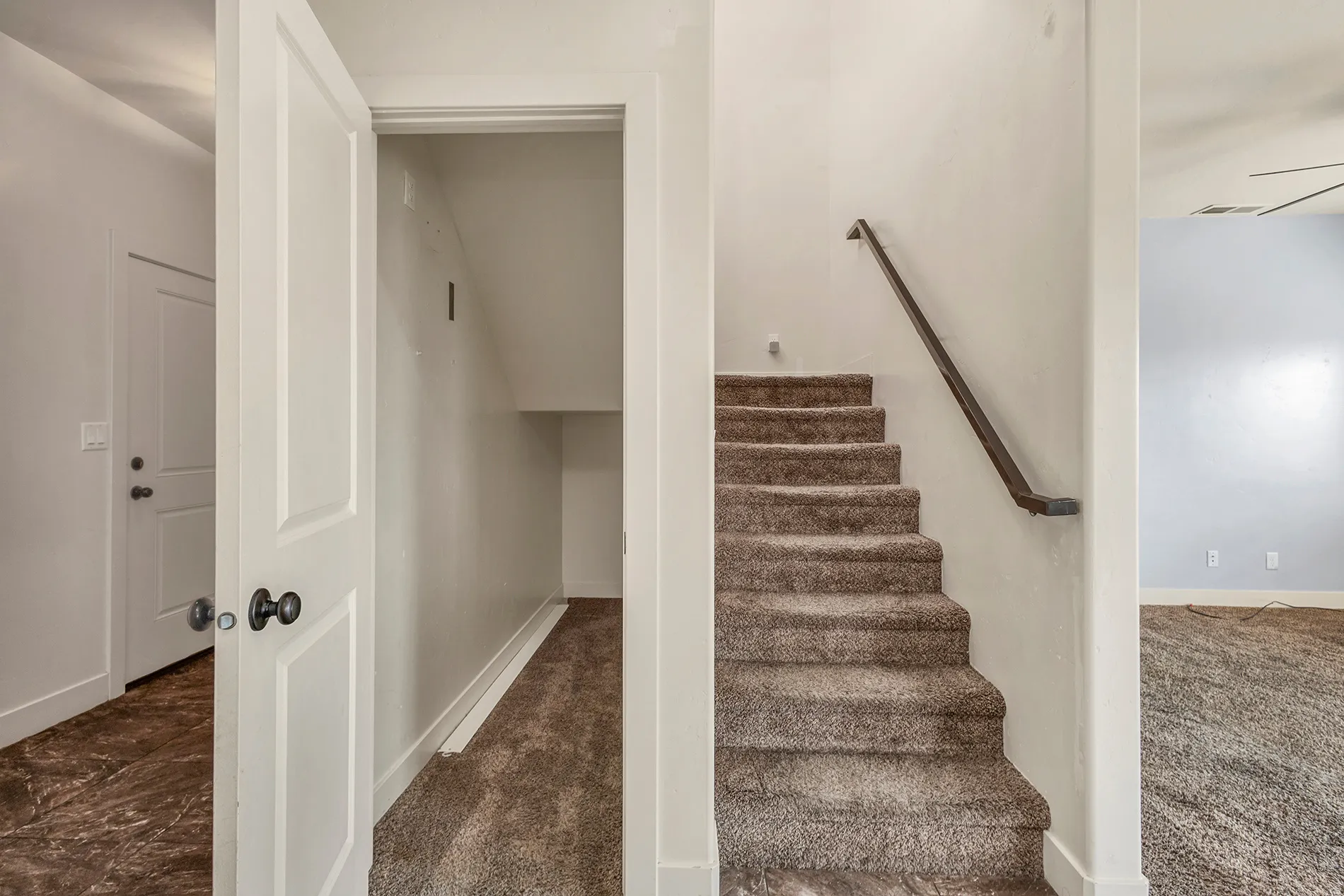 Bright hallway with generous closet storage, carpeted staircase with handrail, and wood-finish flooring in adjacent spaces