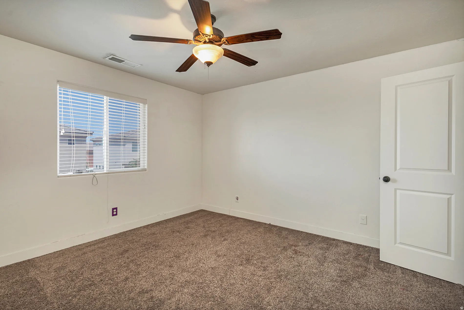 Carpeted flooring, white walls, window with blinds, ceiling fan with light fixture, and white paneled door with dark hardware